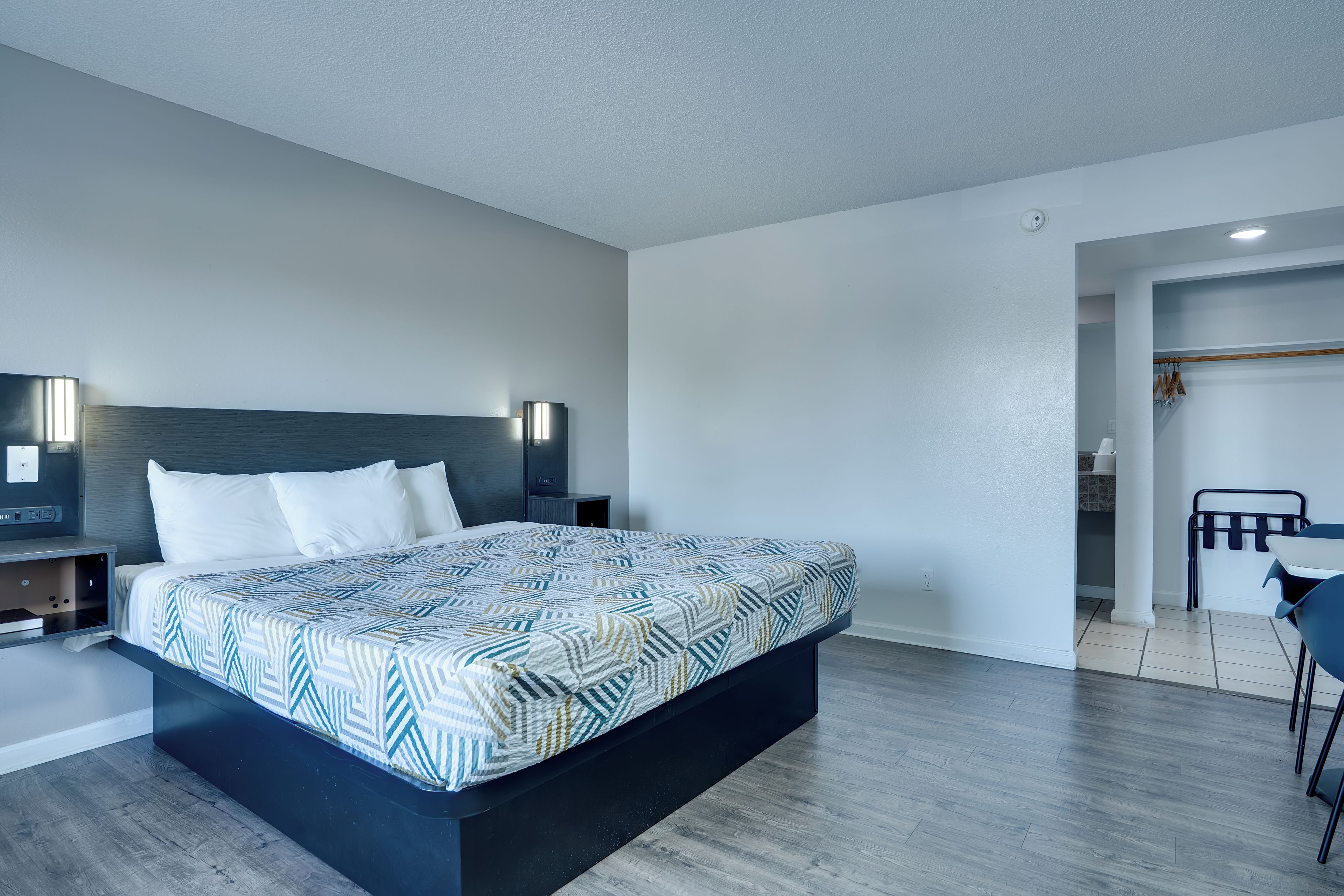 A modern bedroom with a large bed, bedside tables, a wardrobe, and a small seating area.