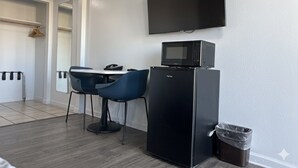 A compact kitchenette with a microwave, a small refrigerator, a flat-screen TV, and a dining area with two chairs.