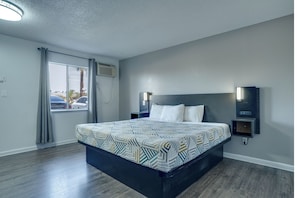 A hotel room with a bed, a nightstand, a wall-mounted lamp, and a window with curtains.