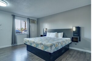 Habitación de hotel con una cama, una mesita de noche, una lámpara de pared y un ventanal con cortinas.