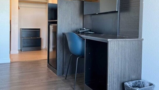 A compact kitchenette with a built-in oven, a small dining area with a blue chair, and a trash bin.