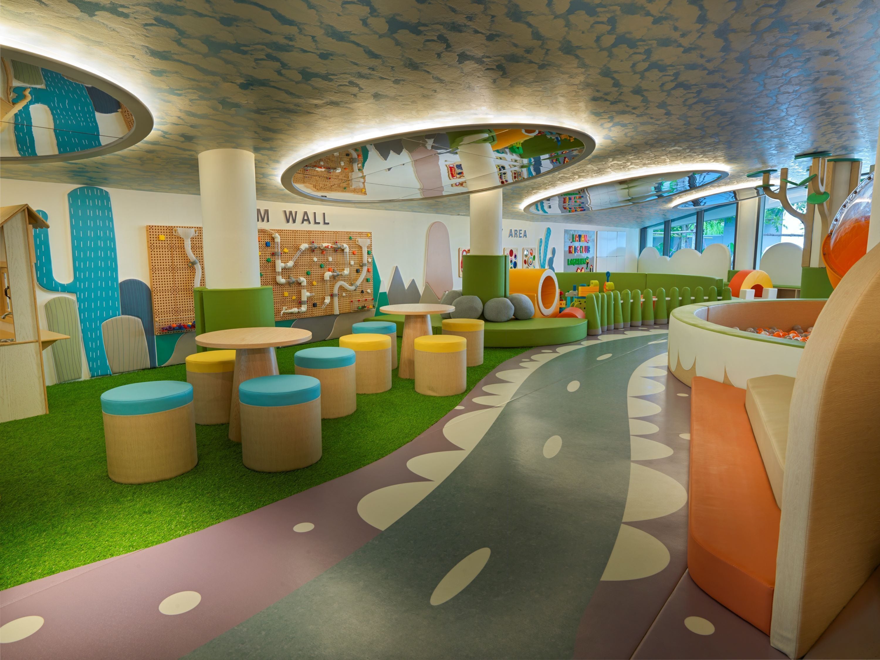 Un espace de jeux pour enfants avec un chemin sinueux, des structures colorées et un mur orné de panneaux éducatifs.