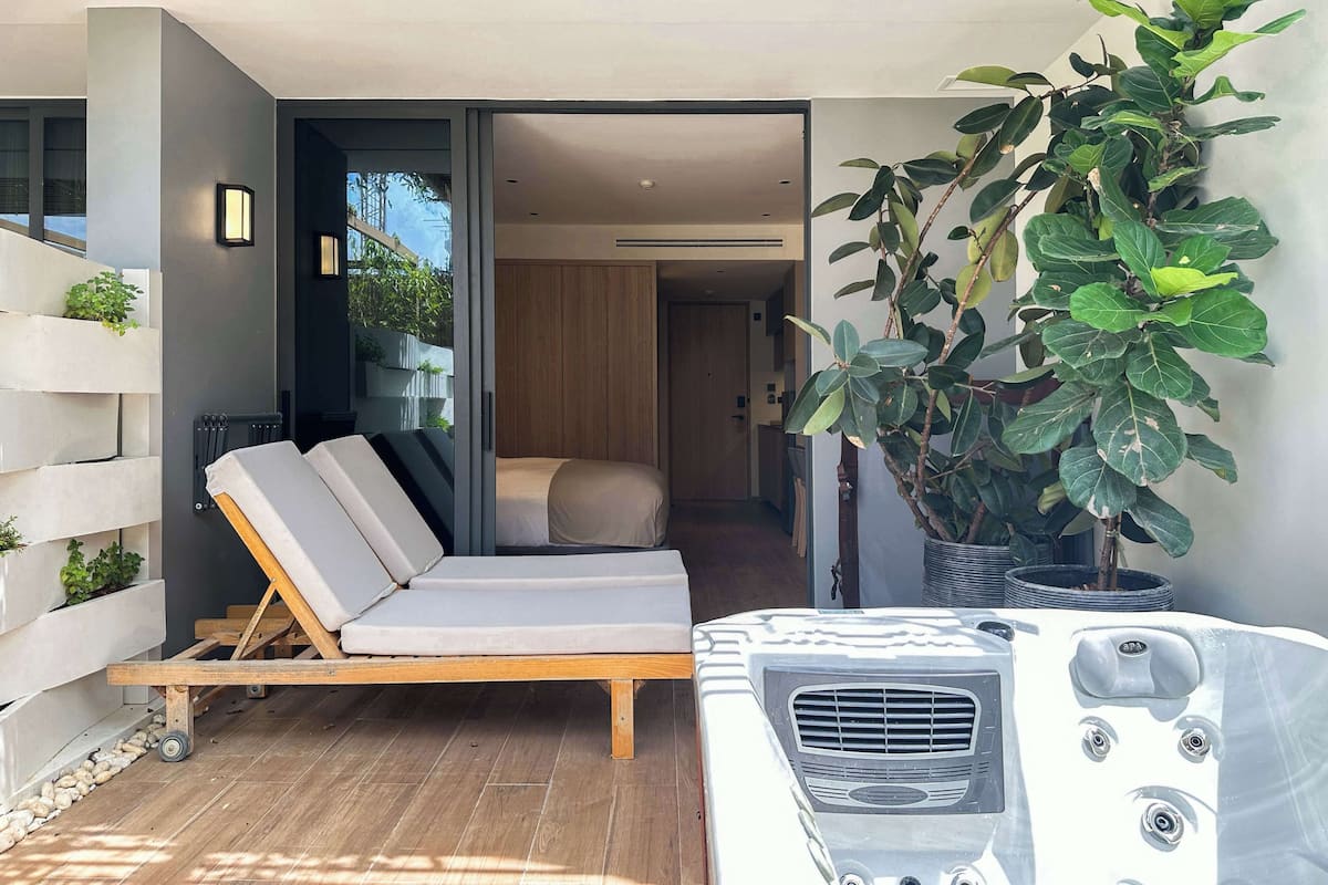 A modern outdoor seating area with a lounge chair, a hot tub, and a potted plant.