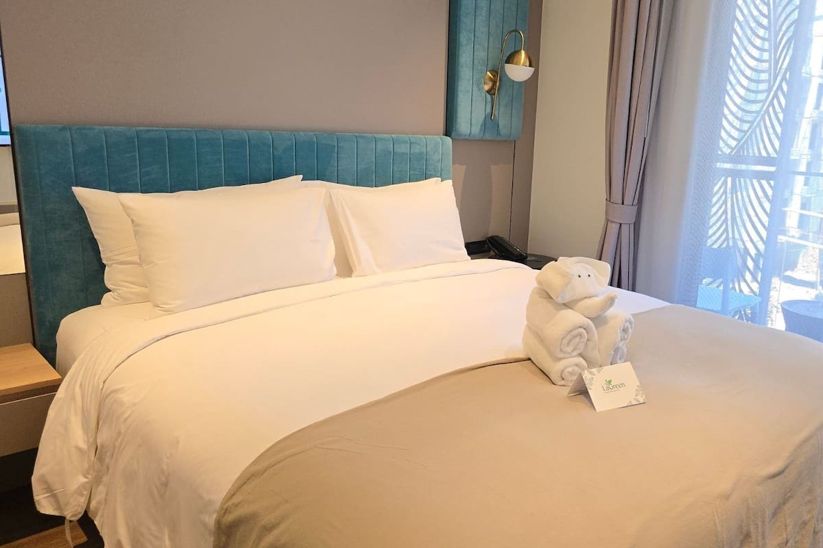 A neatly made bed with white linens, a teal headboard, and a plush white teddy bear with a tag on the bed.