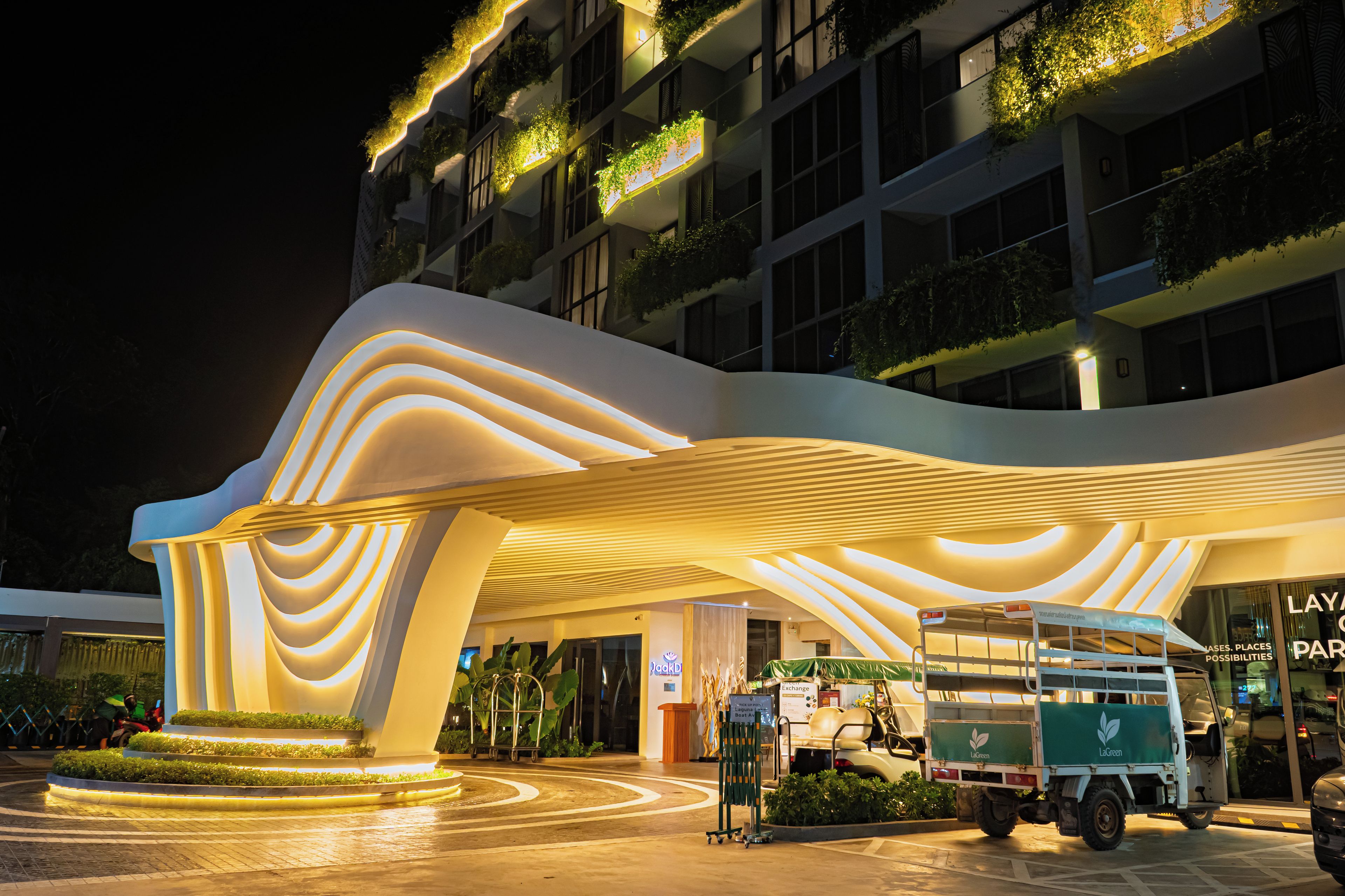 A modern hotel with a unique wavy roof design and illuminated entrance.