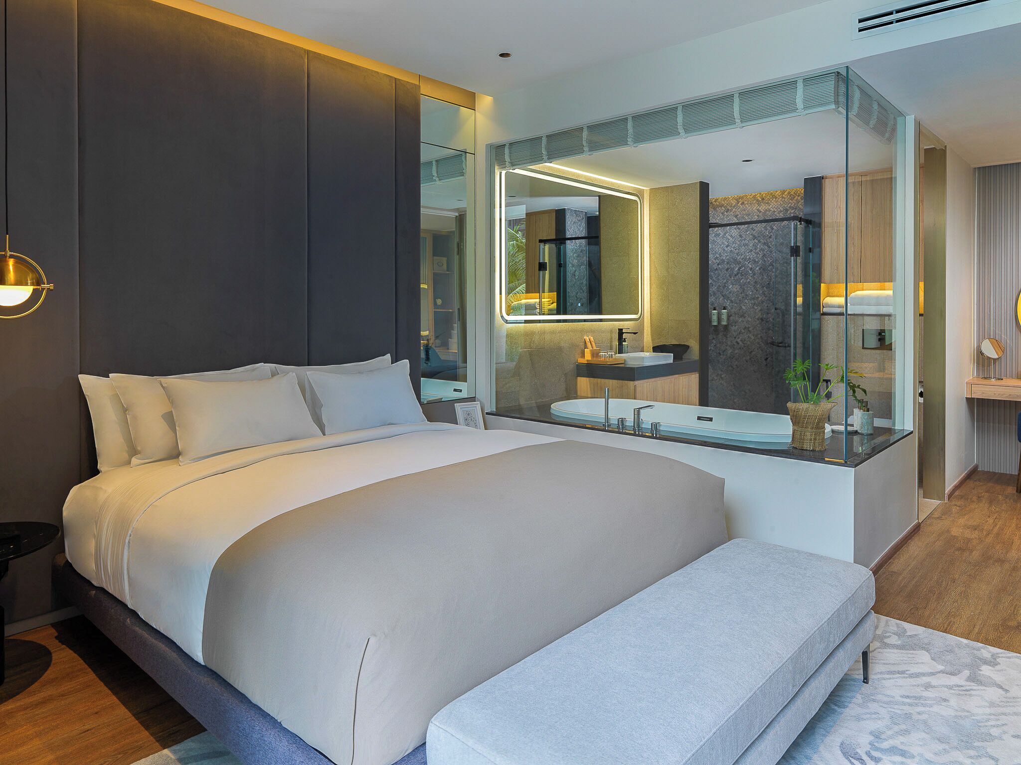 Una habitación de hotel moderna con una cama grande, un baño con paredes de vidrio y vistas a la ciudad.