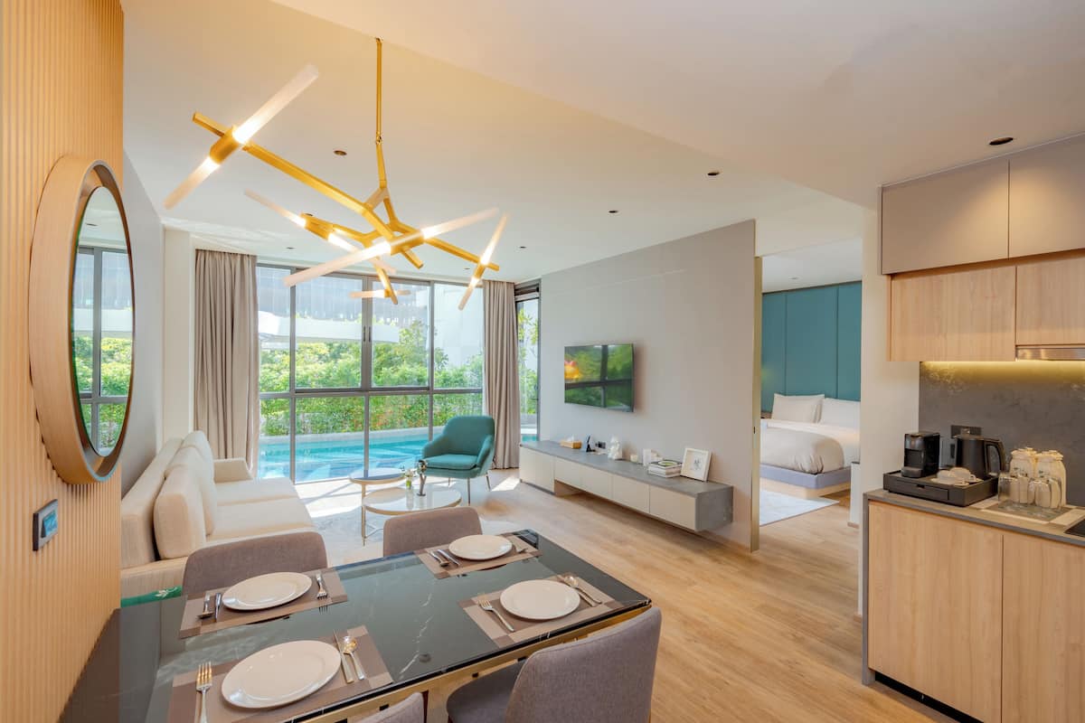 A modern hotel room with a dining area, a sofa, a TV, and a kitchen area.