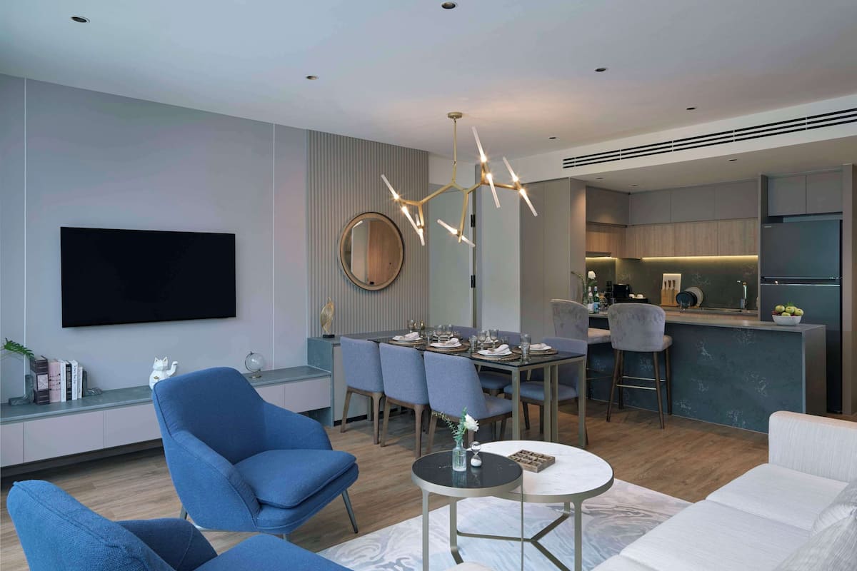 A modern living room with a dining area, a kitchen in the background, and a large flat-screen TV mounted on the wall.