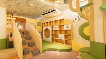 A children's play area with a climbing structure, storage shelves, and a soft play floor.