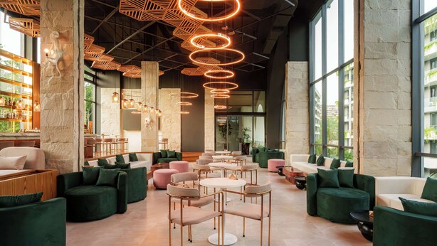 A modern lounge area with round tables and green sofas, large windows, and a stone wall. - La Green Hotel & Residence (Choeng Thale)