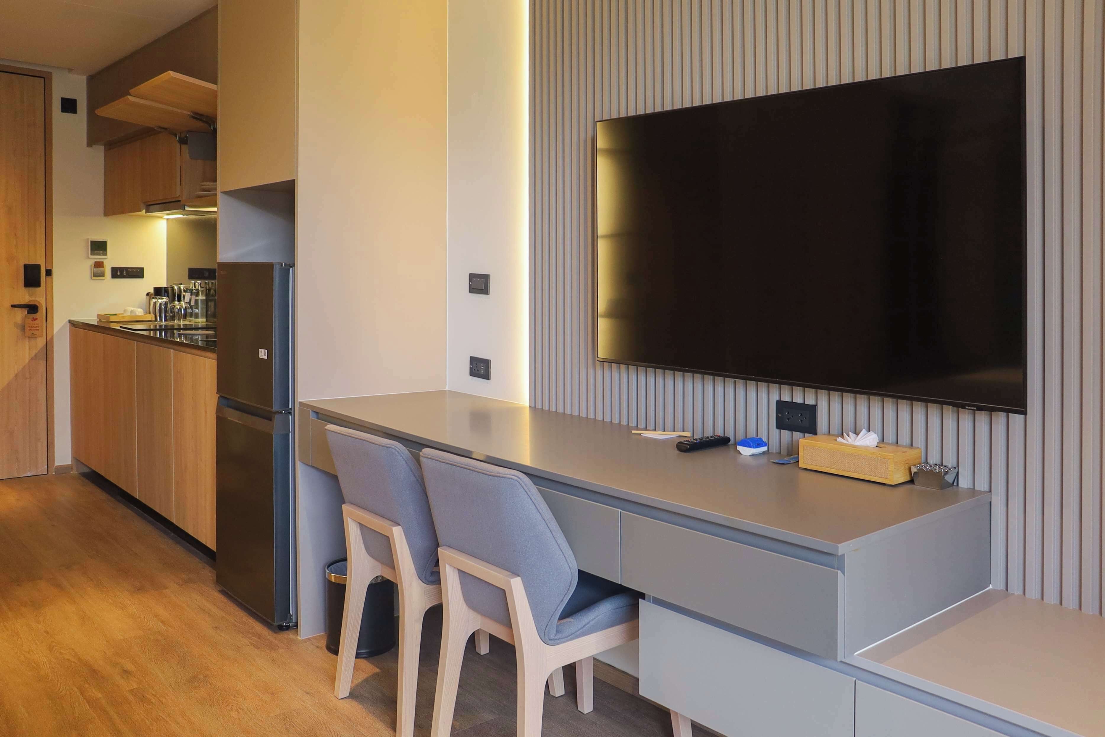Una cocina moderna con armarios de madera, un refrigerador de acero inoxidable y un televisor de pantalla plana montado en la pared.