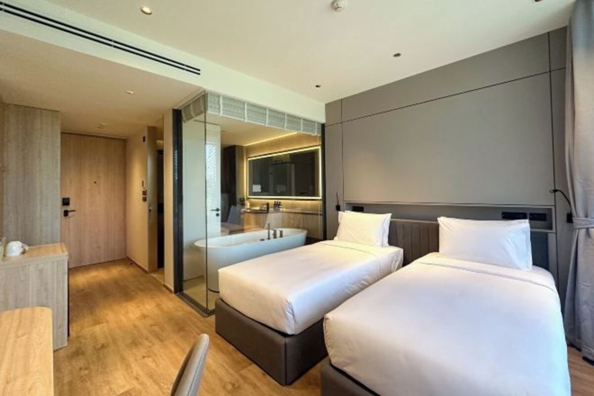 A modern hotel room with two beds, a sitting area, and a bathroom with a bathtub.