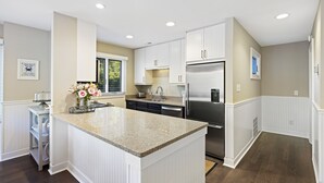 A modern kitchen with white cabinetry, a granite countertop, and stainless steel appliances.