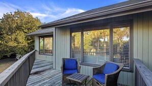 A covered outdoor deck with wicker chairs and a small table, overlooking a body of water and trees.