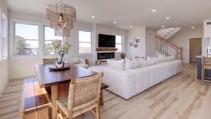 Un salon spacieux avec un grand canapé blanc, une table à manger en bois et des chaises en osier.