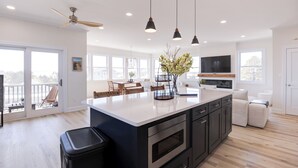 Une cuisine moderne dotée d’un grand îlot central, de meubles de couleur noire et de luminaires suspendus.