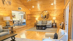 A cozy cabin interior with wooden walls, a round mirror, a fireplace, and a dining area. - Relaxing Lake Hamilton Home with Private Dock, Hot Tub, Kayaks, Fire Pit (Royal)