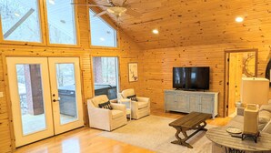 A cozy cabin interior with wooden walls, a large TV, and a dining table. - Relaxing Lake Hamilton Home with Private Dock, Hot Tub, Kayaks, Fire Pit (Royal)