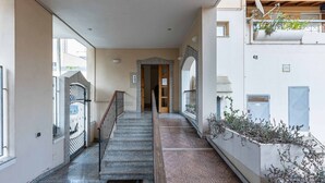 A corridor with a staircase, a door at the end, and a balcony with plants. - GuestHost - Modern apartment of about 55sqm, located on the first floor of a building with a lift (steps to access), can accommodate up to 2 people.The accommodation is located in a central district, served by all the main services: bars, restaurants, su (Cagliari)