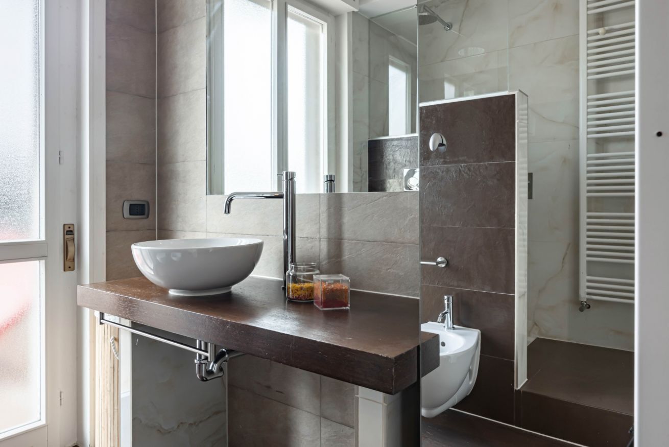 A modern bathroom with a large vessel sink, a mirror, and a walk-in shower.