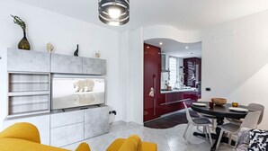 A modern living room with a sofa, a dining table with chairs, a kitchen area, and a TV mounted on the wall. - GuestHost - Modern apartment of about 55sqm, located on the first floor of a building with a lift (steps to access), can accommodate up to 2 people.The accommodation is located in a central district, served by all the main services: bars, restaurants, su (Cagliari)