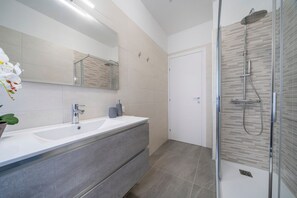 Un baño moderno con un espejo grande, dos lavamanos, una ducha y una planta en maceta.