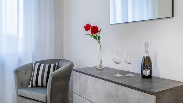 A modern room with a grey sofa, a vase with red roses, two wine glasses, and a bottle of champagne on a grey console table.