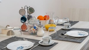 A breakfast setup with plates, cups, a pitcher, and a fruit bowl on a table.