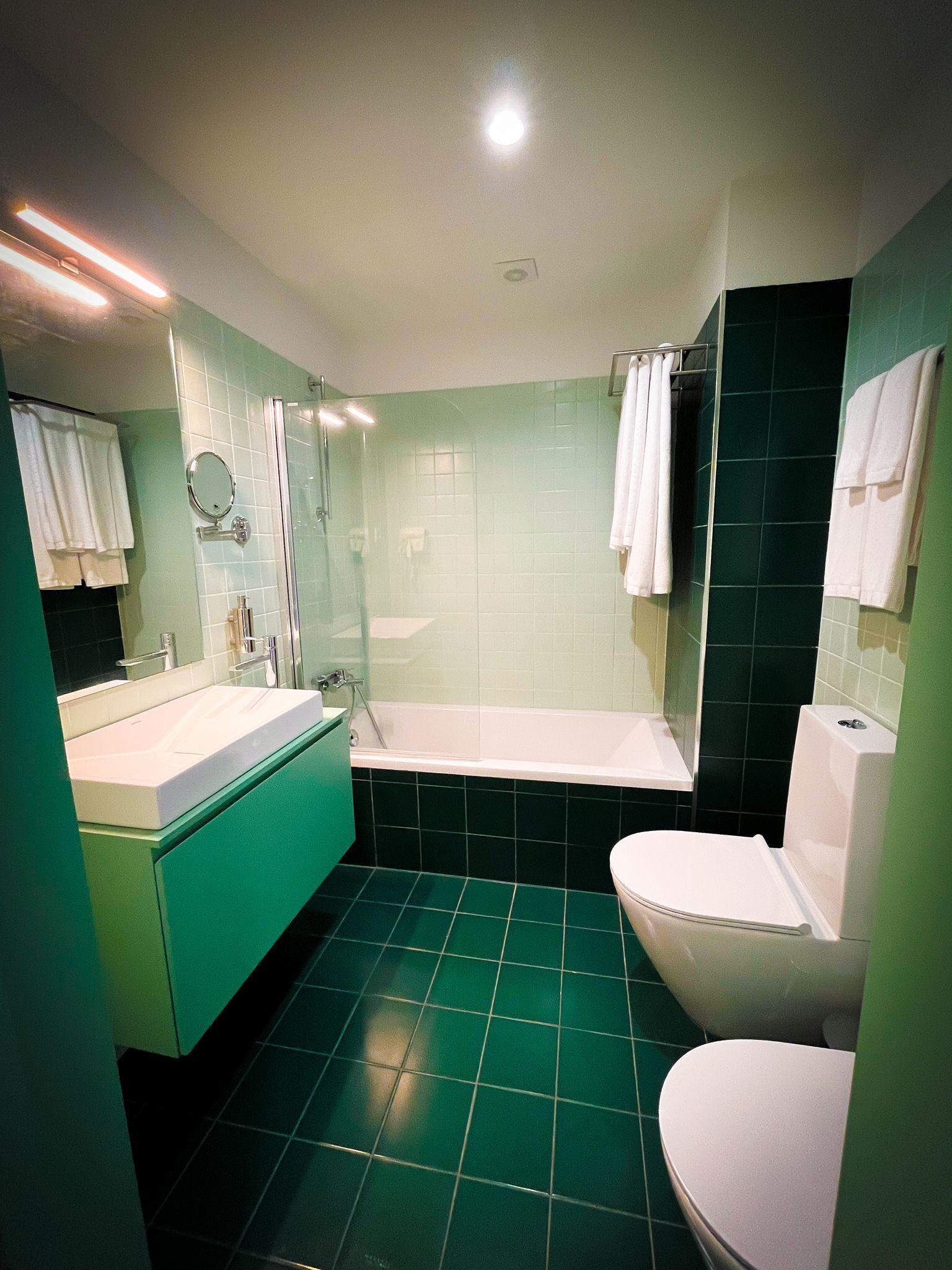 A bathroom with a green-tiled floor, a white sink, a white toilet, and a bathtub with a shower enclosure.