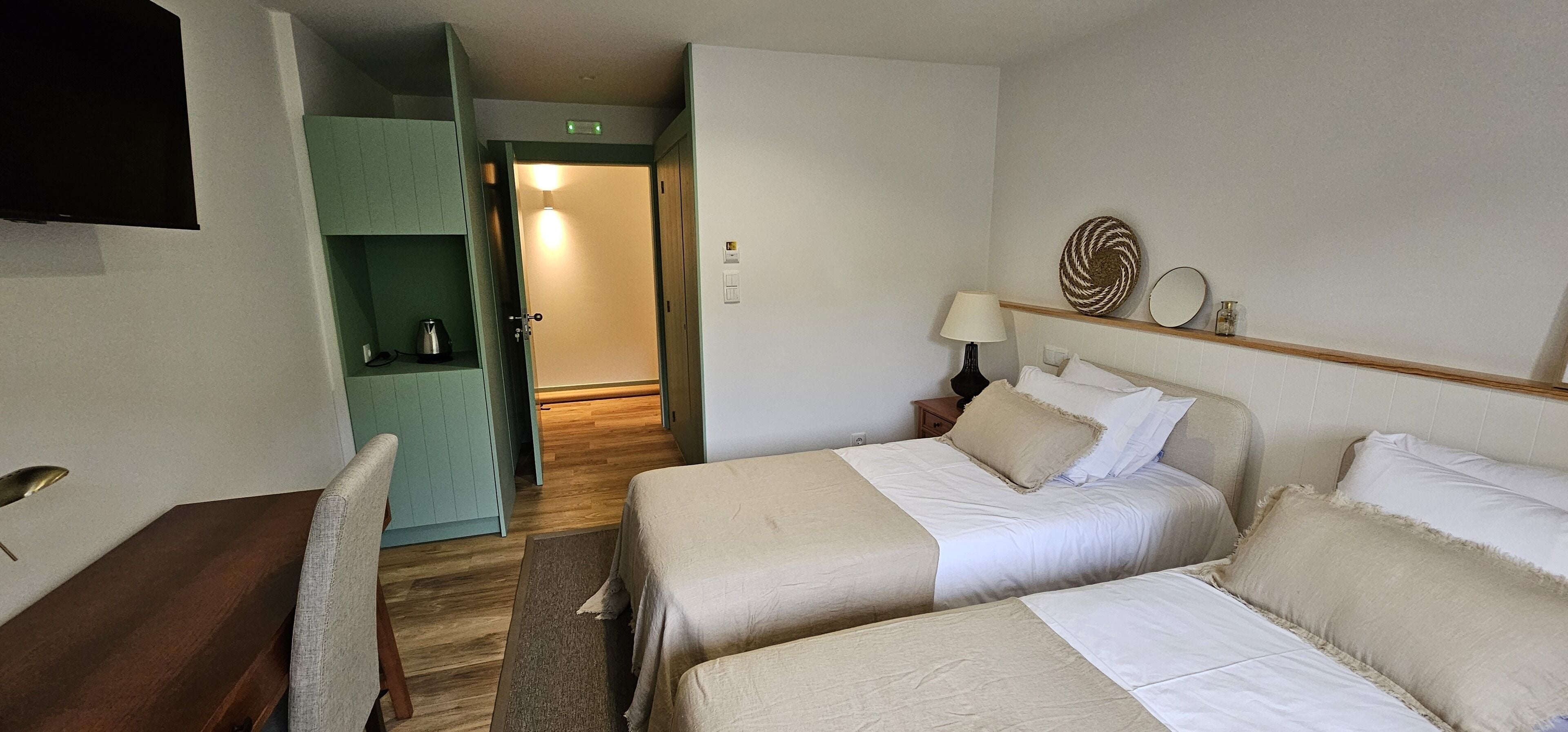 A hotel room with two beds, a desk, a TV, and a green cabinet.