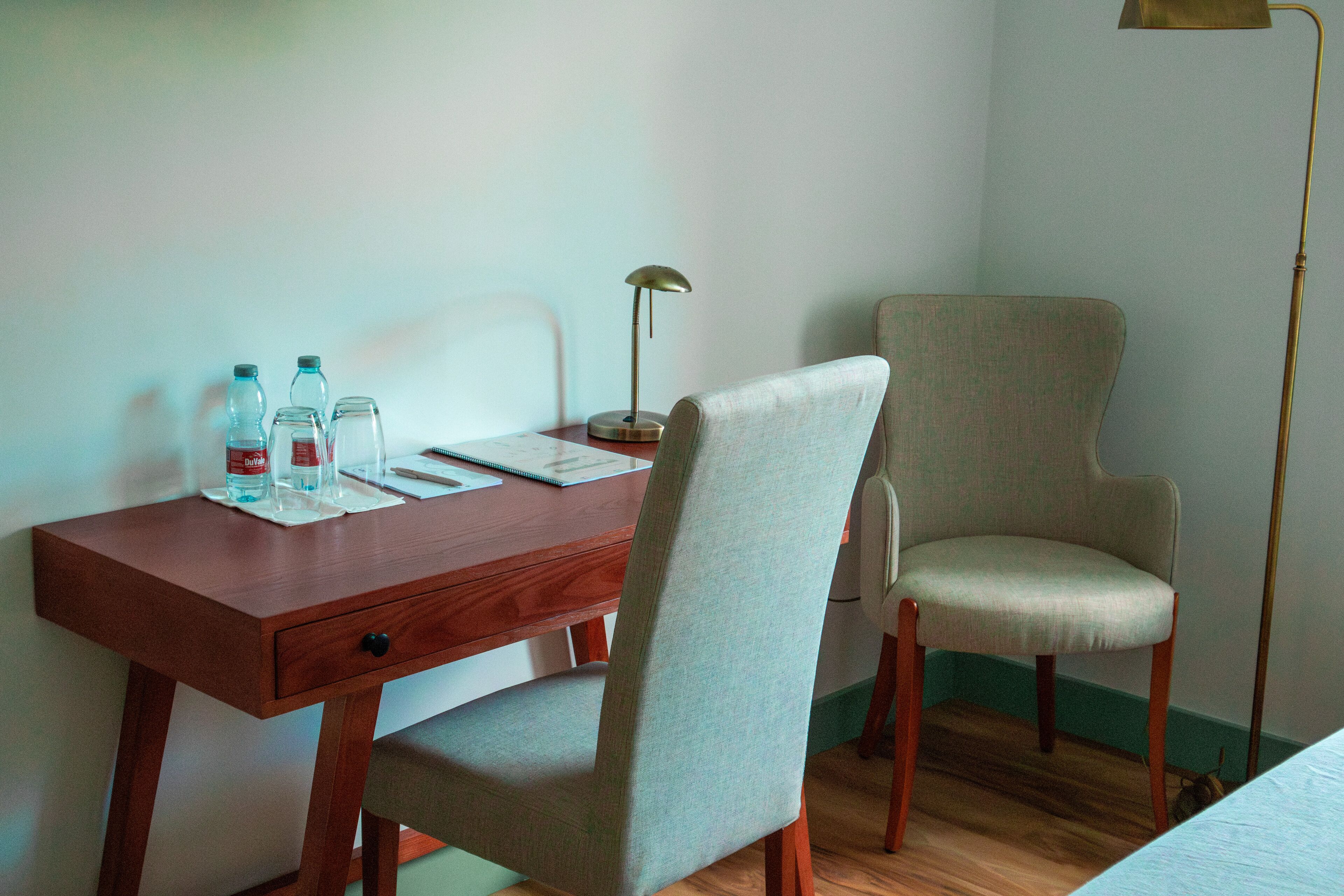 A wooden desk with a chair, a lamp, and a bottle of water.