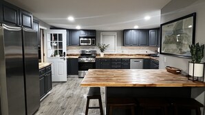 A modern kitchen with dark cabinets, stainless steel appliances, a wooden island, and a grey sofa. - Peaceful Riverfront Cottage with Private Hot tub (Lake Katrine)