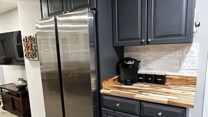 A modern kitchen with dark cabinets, a stainless steel refrigerator, and a wooden countertop. - Peaceful Riverfront Cottage with Private Hot tub (Lake Katrine)