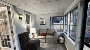 A covered porch with a sofa, a chair, a lamp, and a picture on the wall. - Peaceful Riverfront Cottage with Private Hot tub (Lake Katrine)