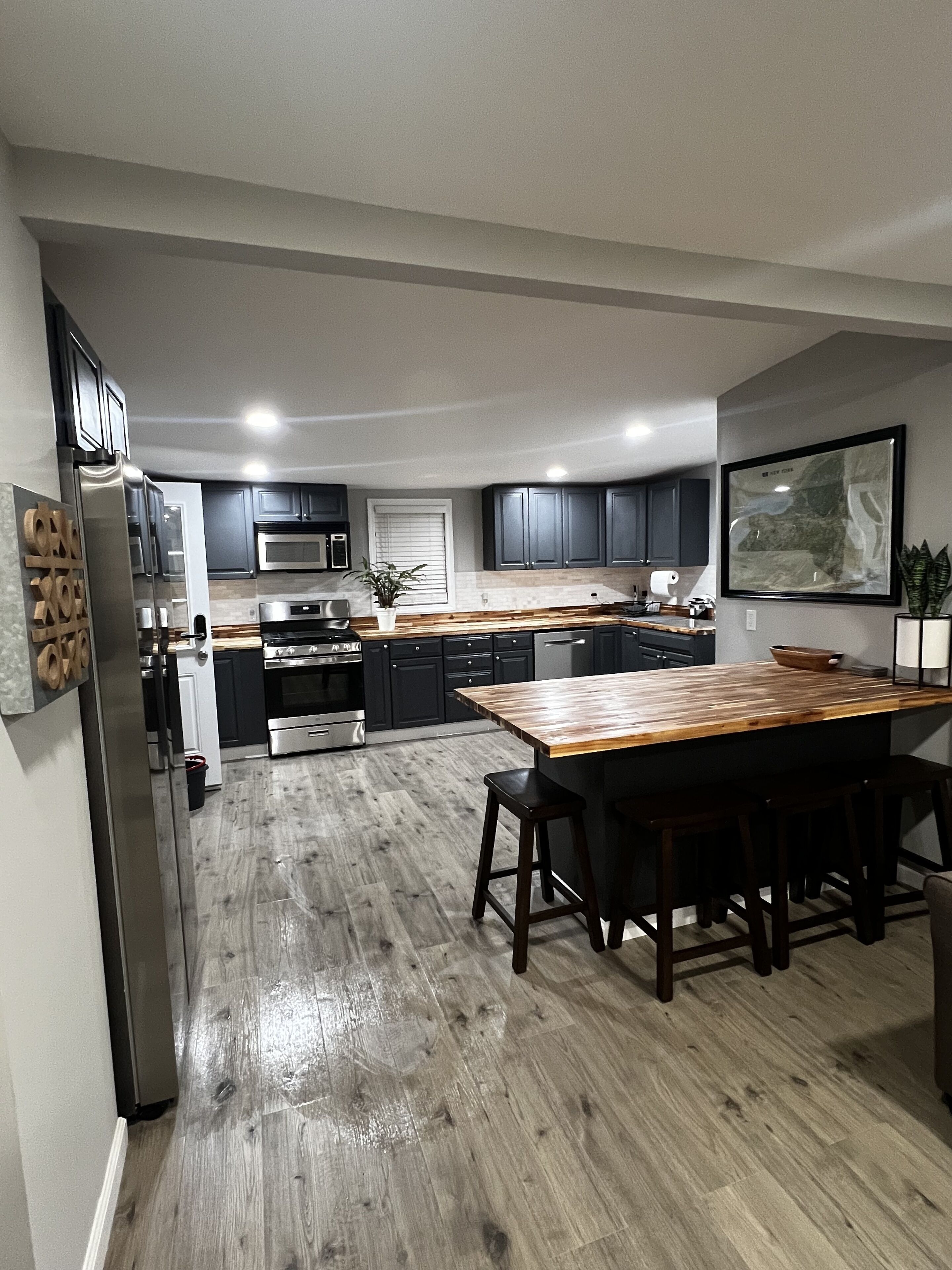 A modern kitchen with dark cabinets, a wooden island, stainless steel appliances, and a large window.