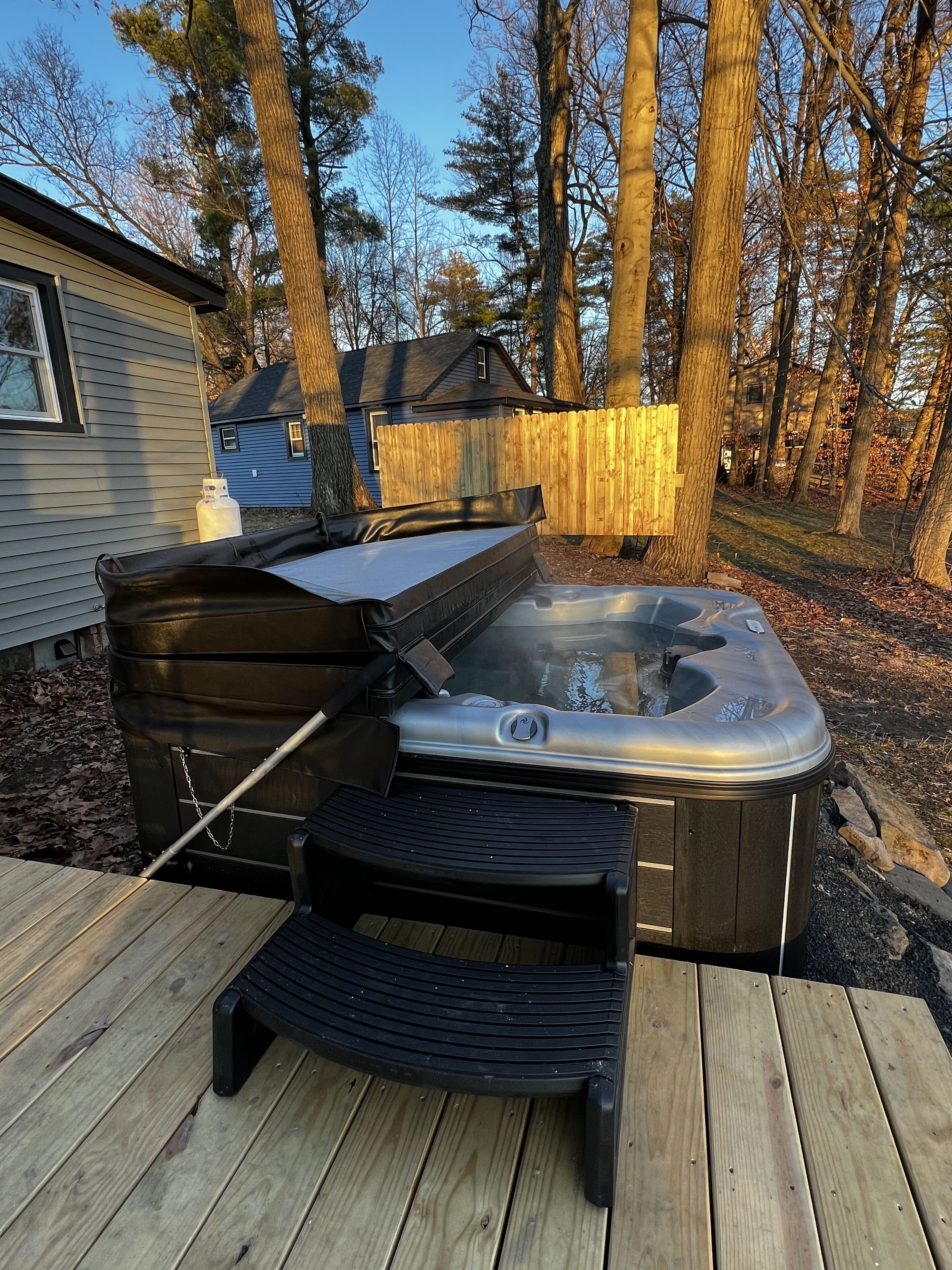 A hot tub on a wooden deck with a wooden fence and trees in the background.