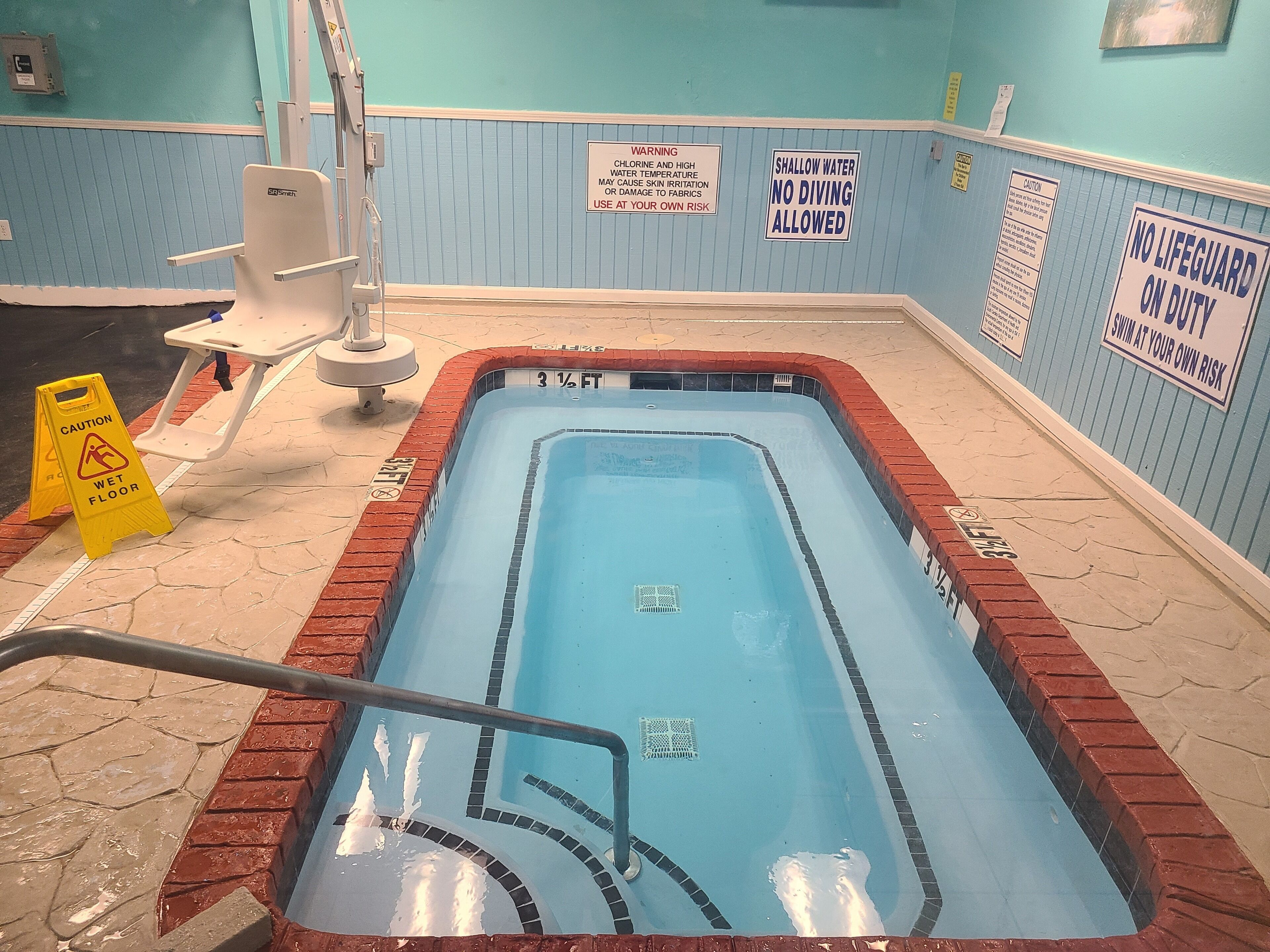 En lille swimmingpool indendørs med sikkerhedsadvarsler og skilt, der angiver lavt vand.