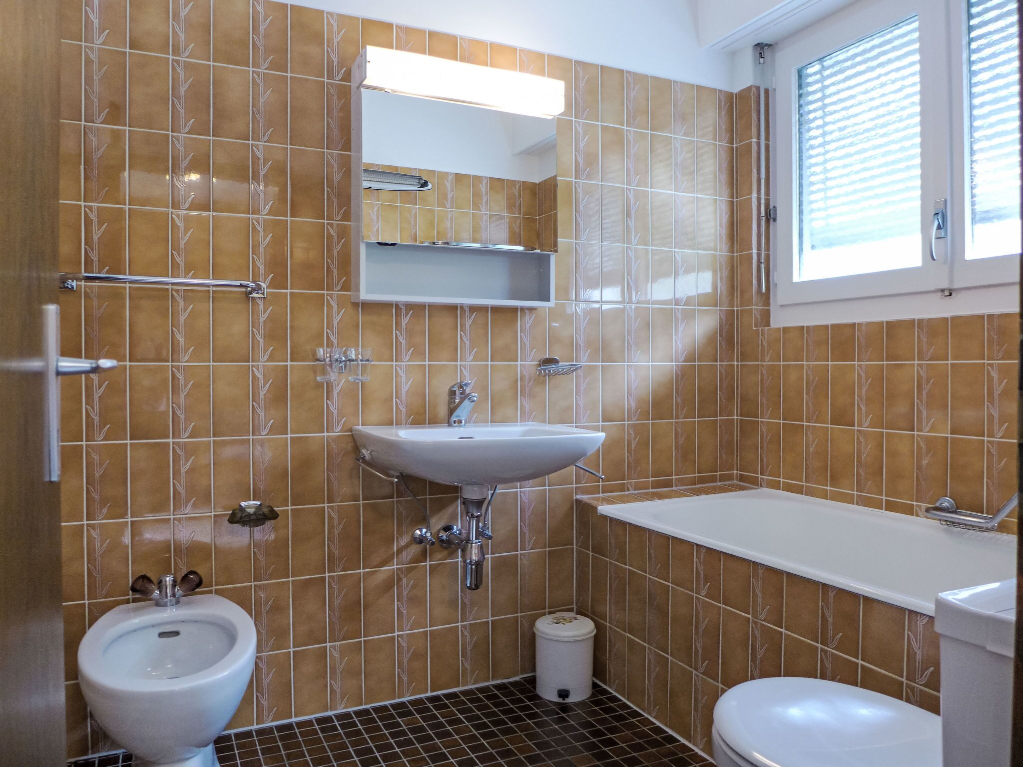 Ein Badezimmer mit Waschbecken, Bidet, Toilette und einem Fenster mit Jalousien.