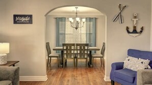 Un comedor con mesa y sillas, una lámpara de araña, un cartel que dice "seaside cottage" y decoración náutica.
