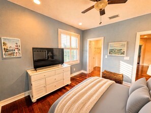 A bedroom with a bed, a dresser, a television, and a ceiling fan.
