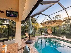 A pool area with a ceiling fan, a hanging chair, and a television screen.