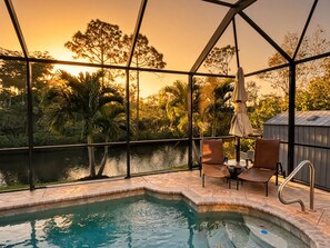 A pool area with a view of trees and a sunset.