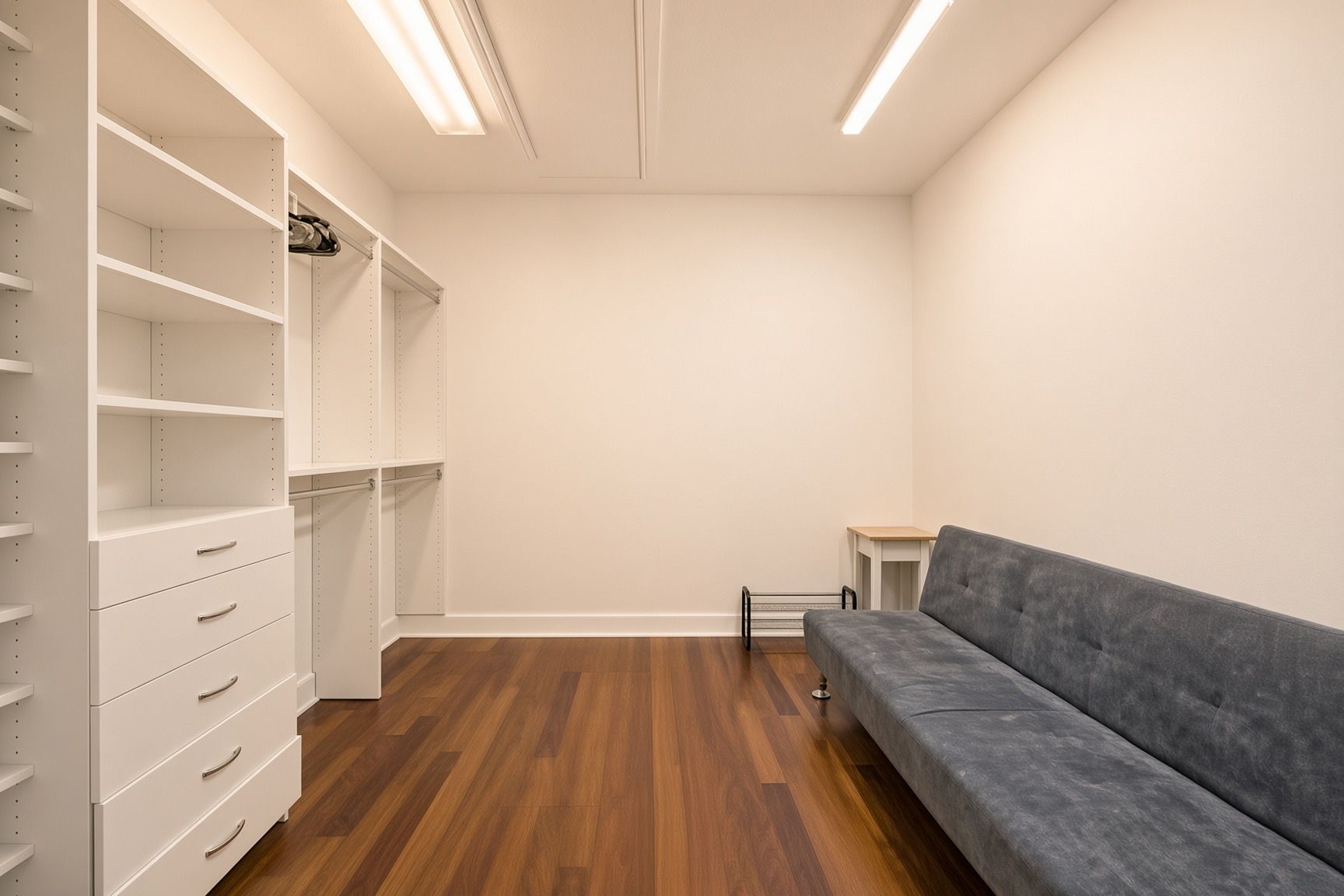 Un dressing ouvert avec des étagères, des tiroirs et un canapé gris.