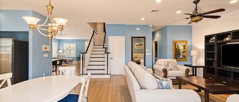 A modern living room with a staircase, a dining area, and a TV stand.