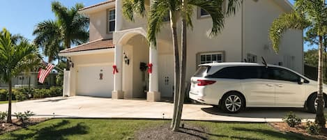 A residential house with a garage, palm trees, and a white car parked in front.