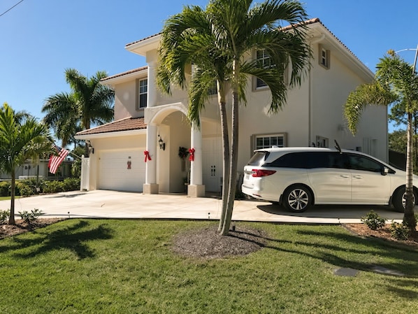 A residential house with a garage, palm trees, and a white car parked in front.