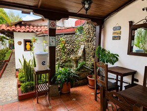 Un patio couvert agrémenté d’un mur en pierre, de plantes en pot, d’une fontaine et d’une table et de chaises en bois.