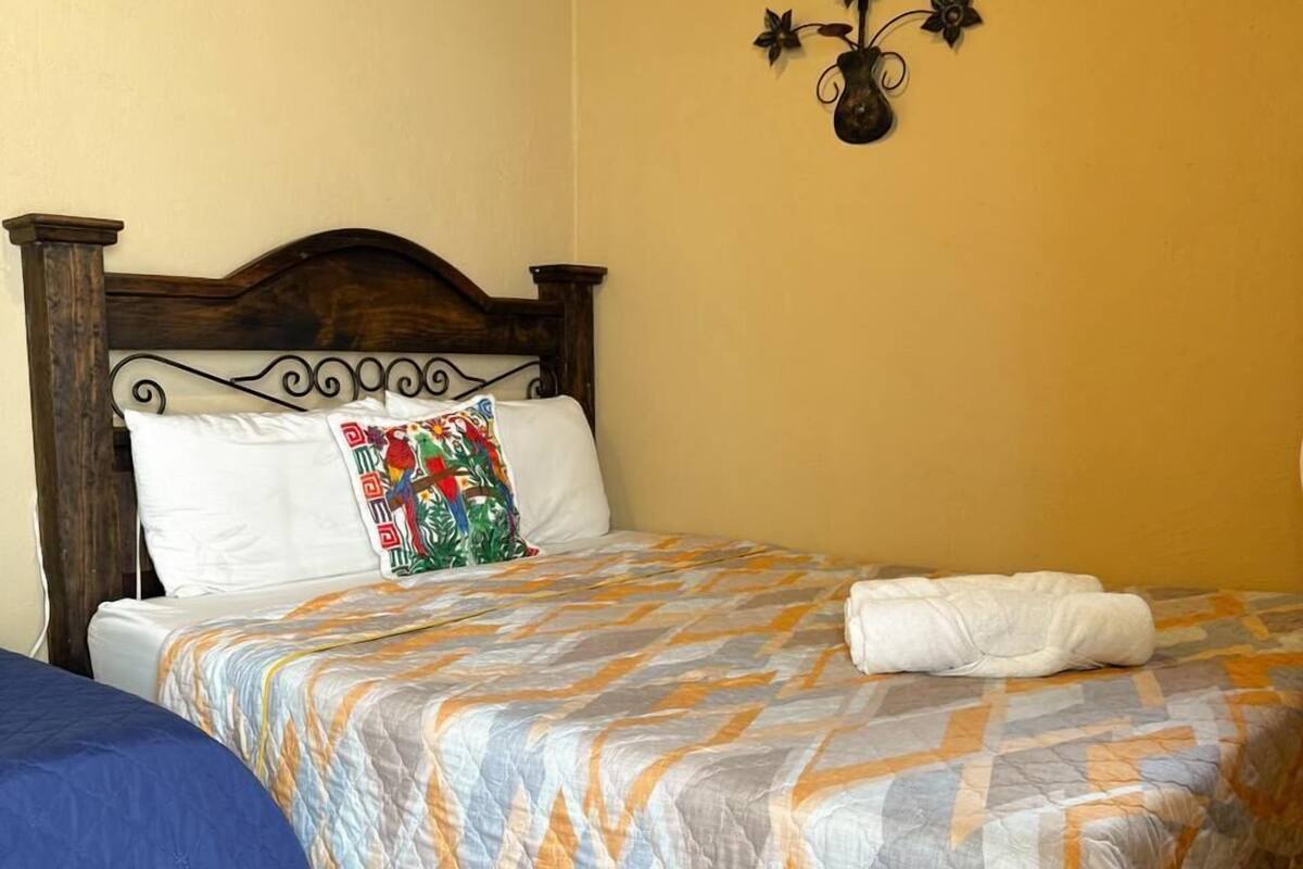 A bedroom with a wooden bed, a blue bedspread, a patterned pillow, and a wall-mounted decoration.