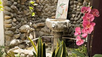 Un muro de piedra con una jardinera colgante, una fuente para pájaros y diversas plantas.