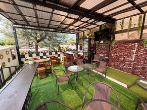 An outdoor patio with wooden tables and chairs, a bar area, and a wall with hanging plants. - Hotel Casa Nikté (Antigua Guatemala)